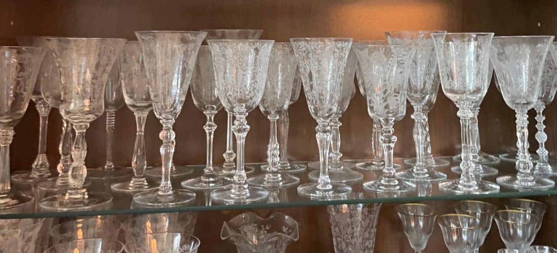Row of crystal drinking glasses lined up on a glass shelf